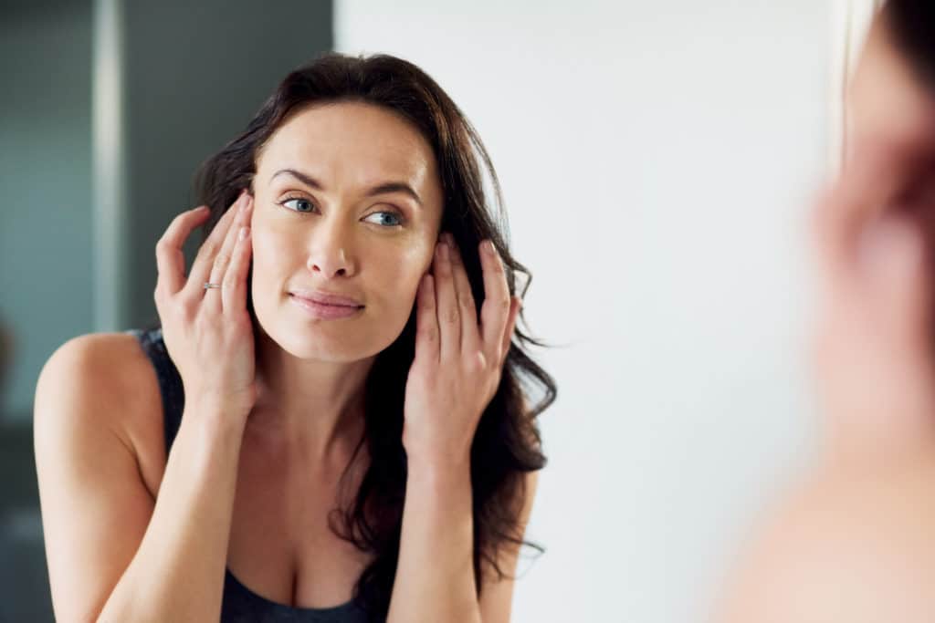 Woman with youthful clear skin looking in mirror